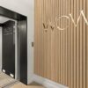 Interior of a beauty clinic with a wooden slat wall featuring a metallic ‘WOW’ logo and an adjacent doorway with a black interior