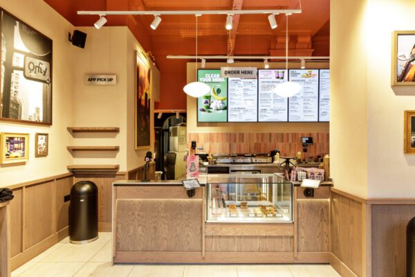 Joe & The Juice service counter with timber panelling and pastry display, below an ornate plaster ceiling painted terracotta, High Holborn.