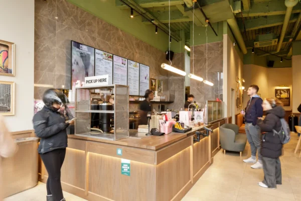 Order pick-up point and servery counter at Joe & The Juice Wimbledon with customers waiting